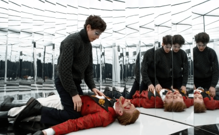 The mime straddling an unconscious Joker in the hall of mirrors.